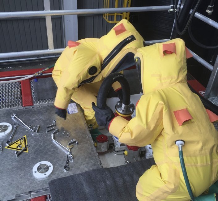 Two operators in gas-tight protective suits connecting an HF transfer hose